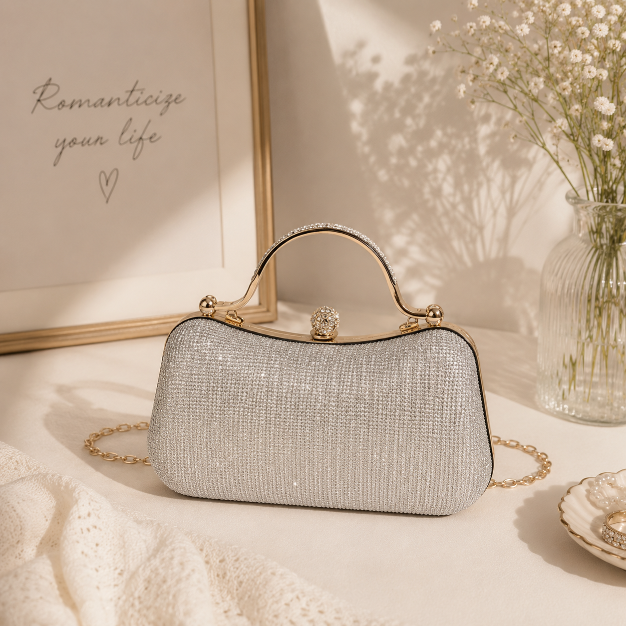 Silver crystal evening clutch bag with a structured silhouette, polished metal top handle, detachable chain strap, and sparkling embellished exterior on a white background.