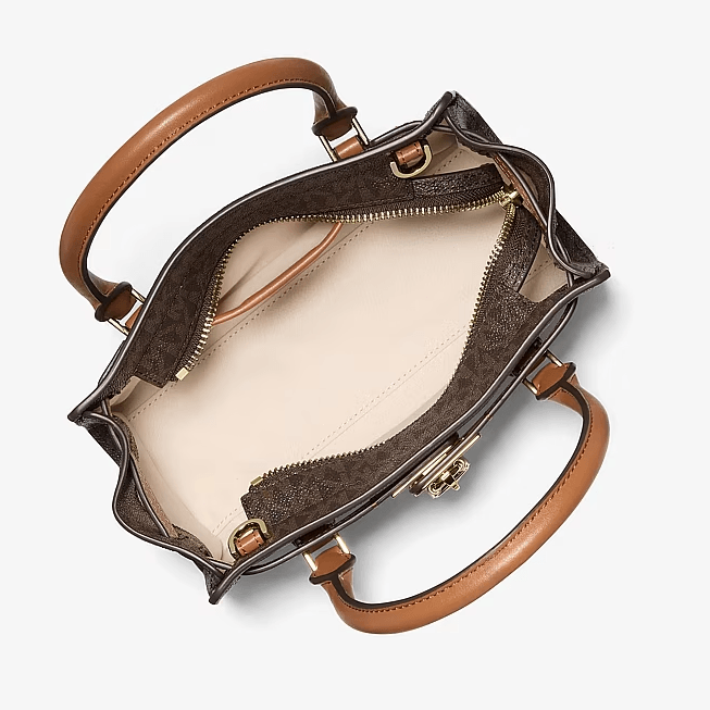 An overhead view of a structured handbag showing its interior, featuring dark brown patterned fabric, tan leather handles, and a cream-colored lining.